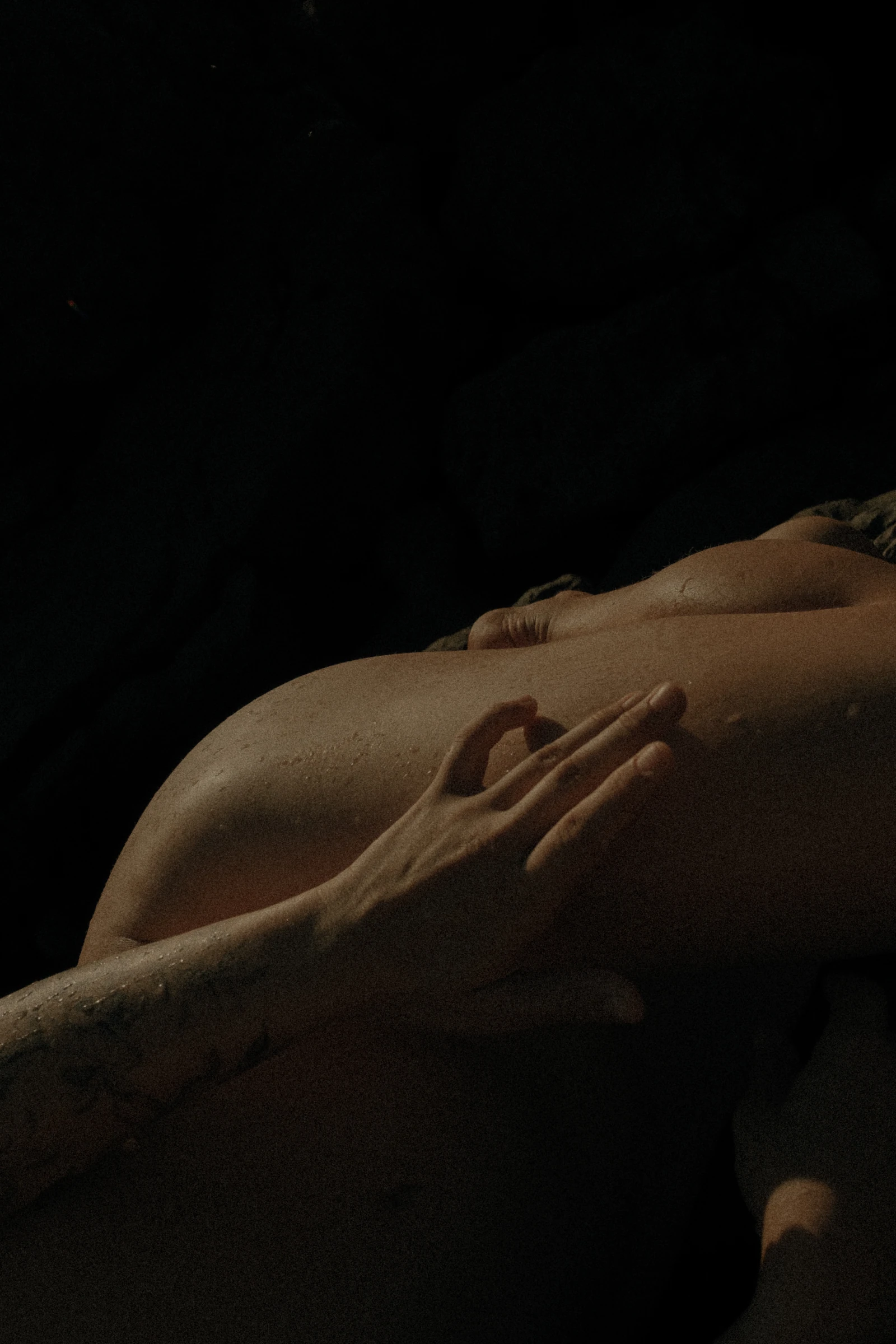 A hand rests on wet skin in warm, low light.