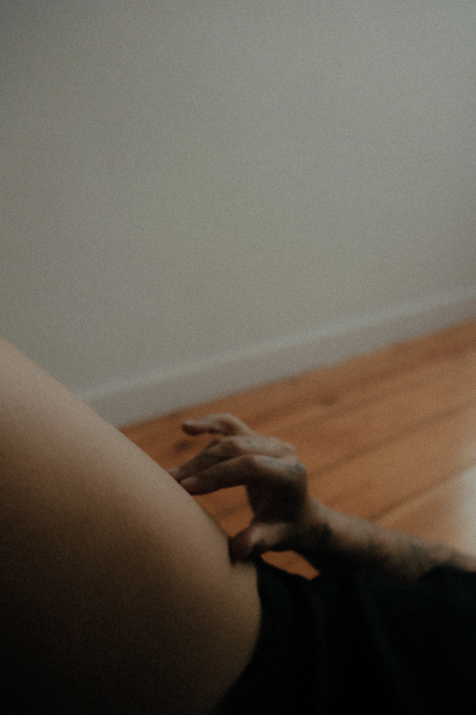 A softly blurred hand and the curve of a body beside a wooden floor.