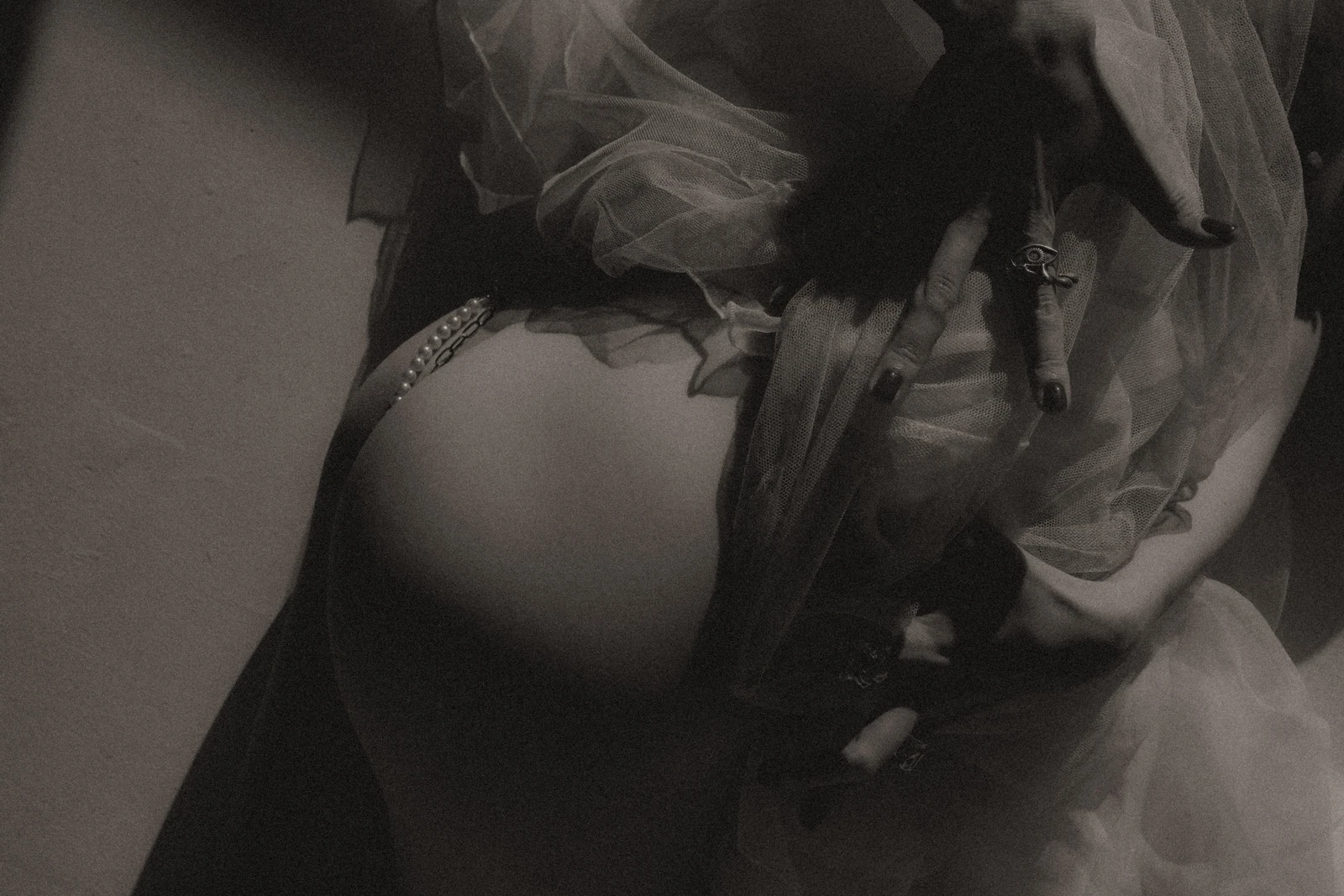Hands, a ring and pearls rest against gathered sheer fabric in monochrome.